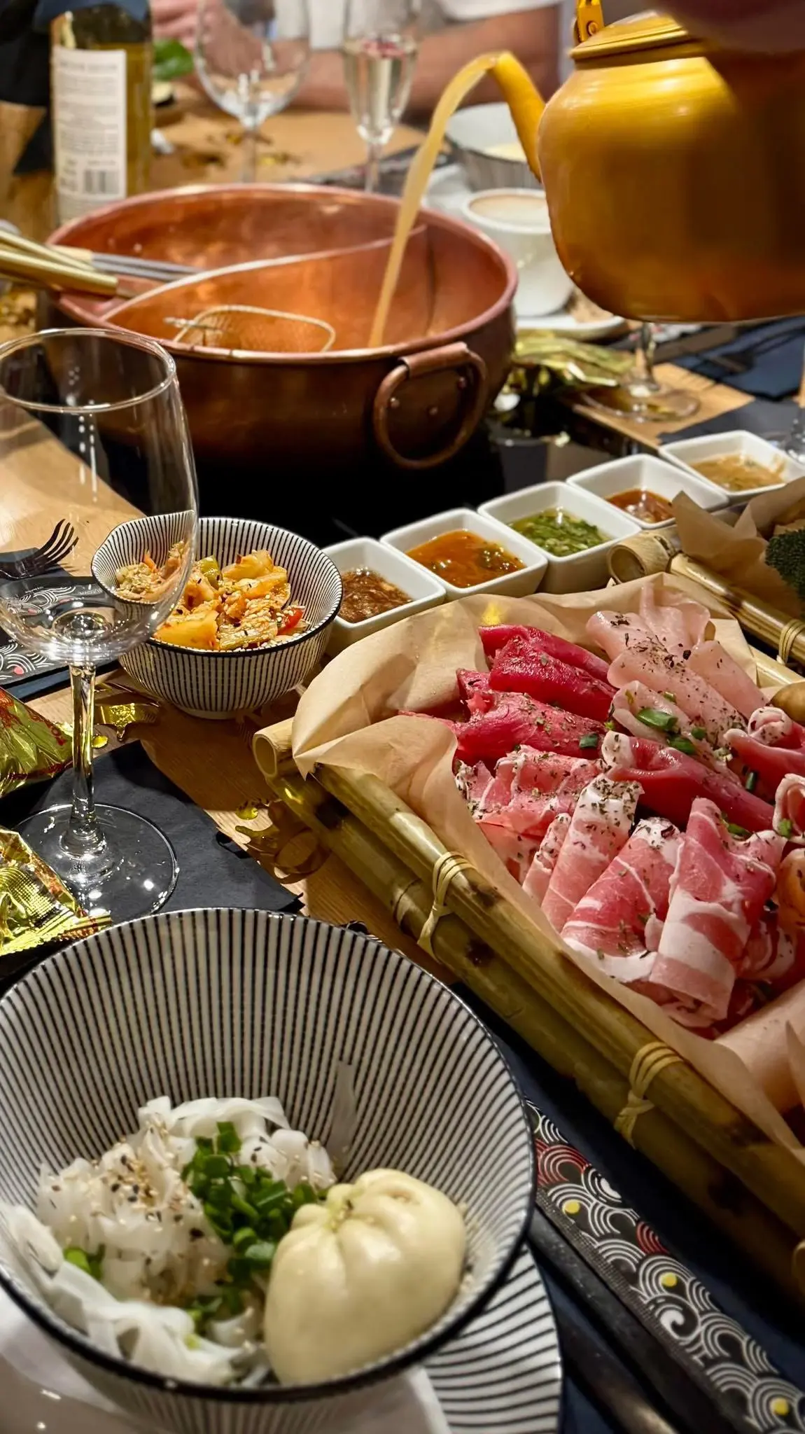 Hot pot przy stole – miedziany garnek z bulionem, świeże składniki i sosy.